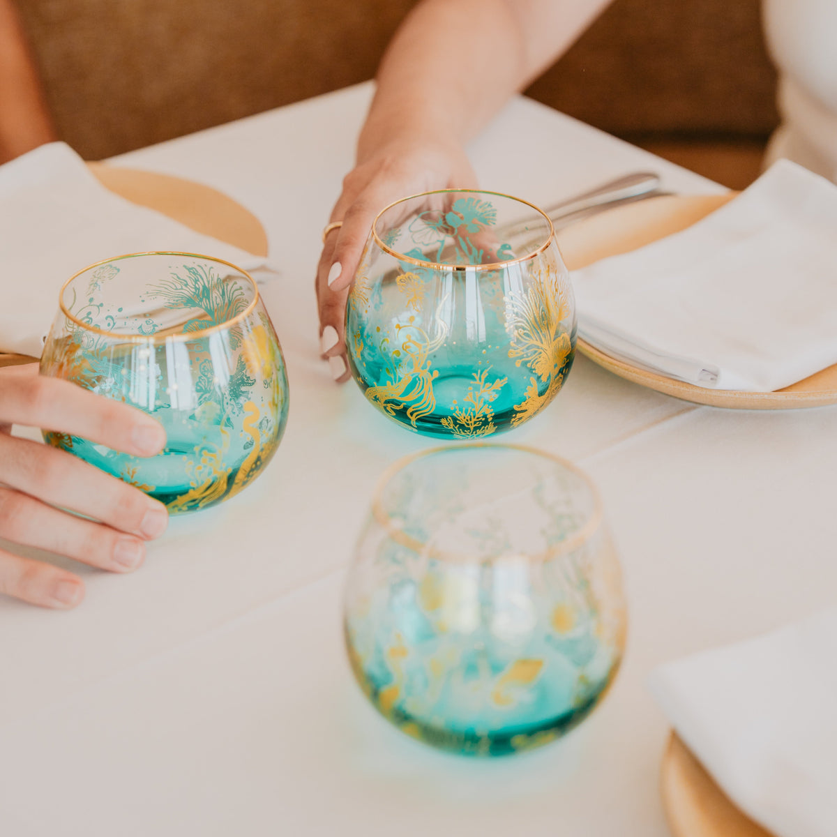 Three beautiful stemless wine glasses held by hands. Elevating dining table. 