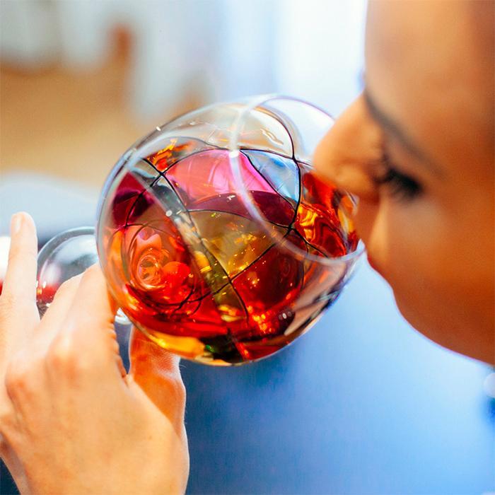 Woman smelling from a luxury hand-painted full brandy glass inspired by the designs of Antoni Gaudi and Sagrada Familia. Cornet Barcelona. Detail colours. 