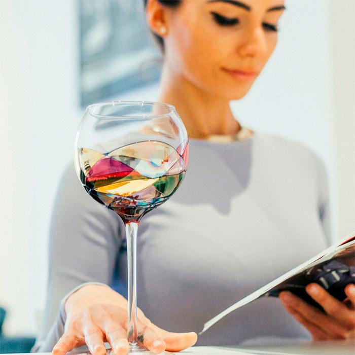 Woman holding a luxury hand-painted tall wine glass inspired by the designs of Antoni Gaudi and Sagrada Familia with wine inside. Detail colours. Cornet Barcelona